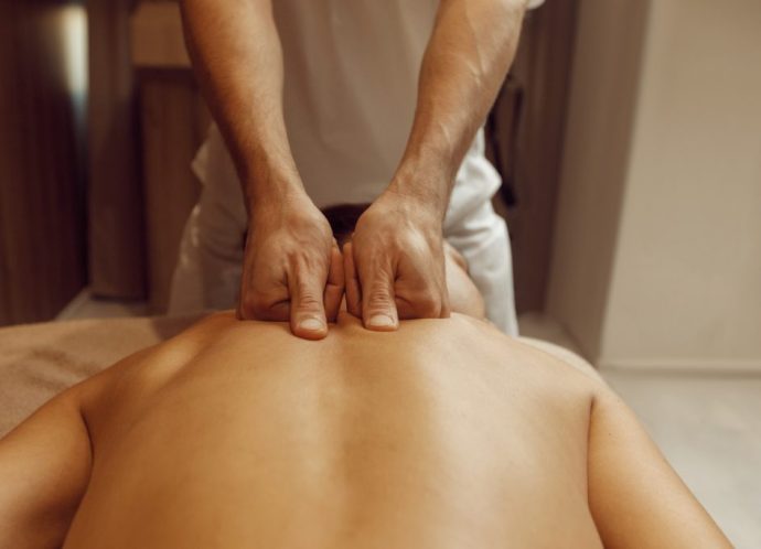 Male masseur rubbing back to slim woman, massage