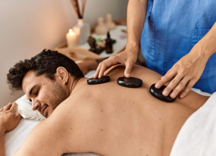 Man reciving back massage with black stones at beauty center.